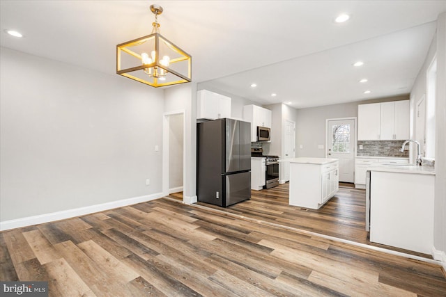 kitchen with a center island, stainless steel appliances, backsplash, a sink, and wood finished floors