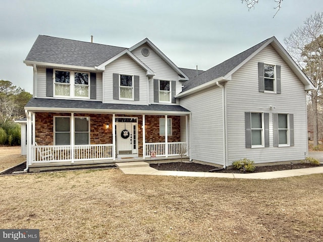 traditional-style home featuring covered porch, a shingled roof, and a front lawn