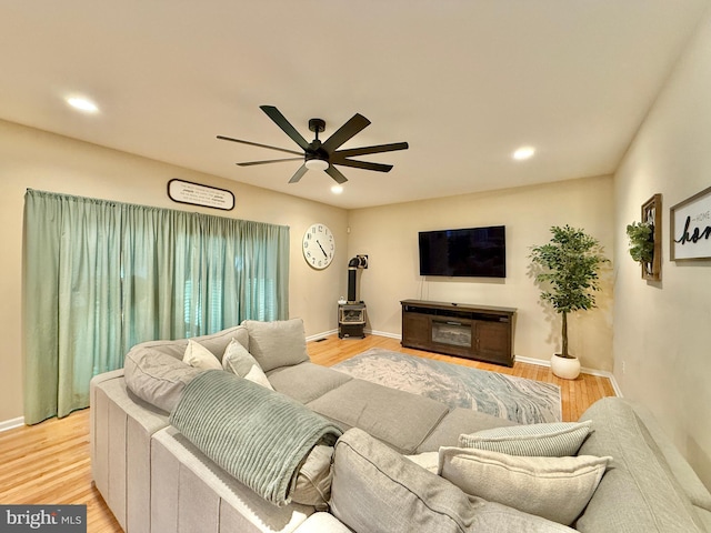 living room featuring light wood finished floors, recessed lighting, a wood stove, ceiling fan, and baseboards