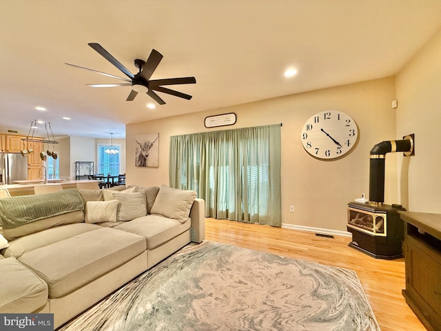 living area with ceiling fan, recessed lighting, baseboards, light wood finished floors, and a wood stove