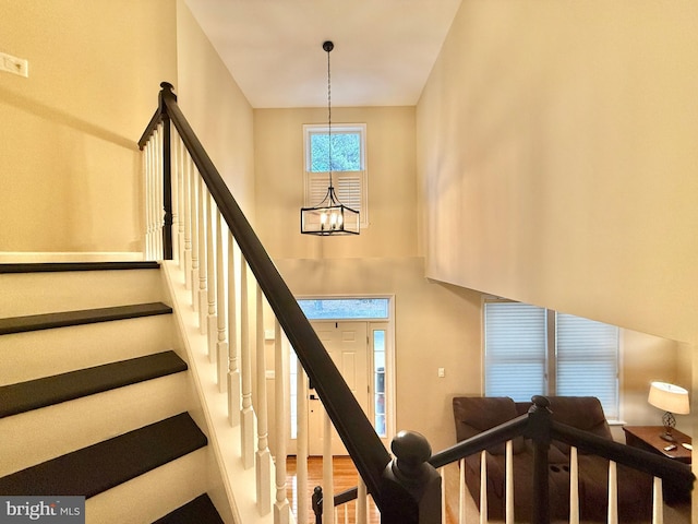 staircase with a high ceiling, wood finished floors, and an inviting chandelier