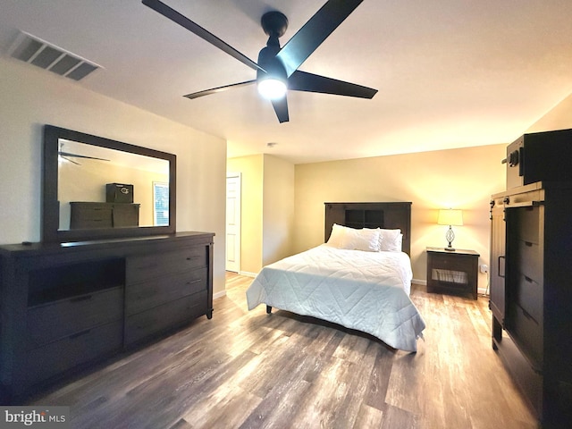 bedroom with ceiling fan, wood finished floors, visible vents, and baseboards