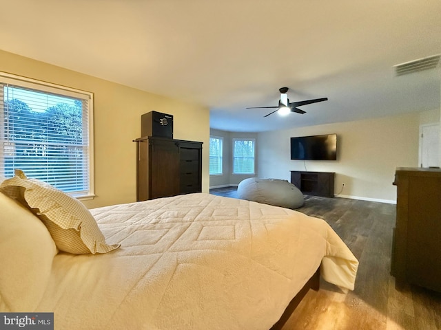 bedroom featuring a fireplace, visible vents, a ceiling fan, wood finished floors, and baseboards