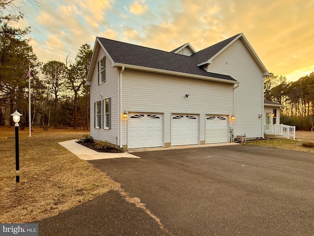 property exterior at dusk with an attached garage, a shingled roof, and aphalt driveway