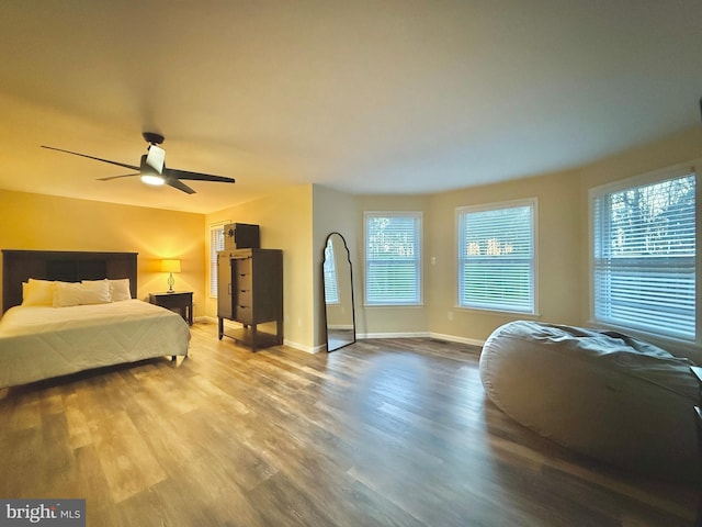 bedroom with ceiling fan, multiple windows, baseboards, and wood finished floors