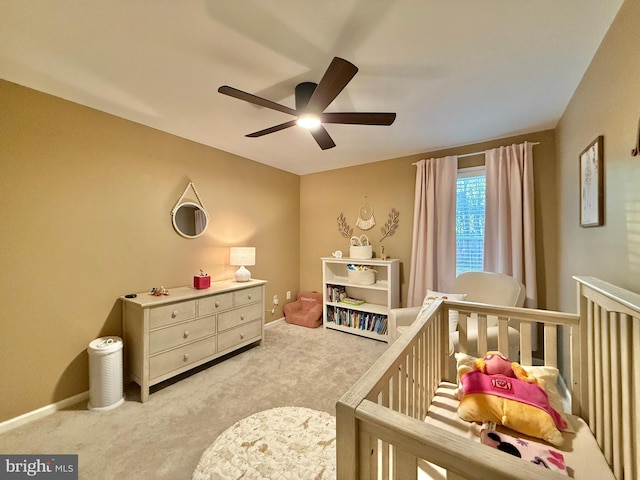 bedroom featuring a nursery area, ceiling fan, baseboards, and light colored carpet