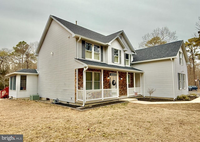 traditional-style home with a front yard, covered porch, central AC, and roof with shingles