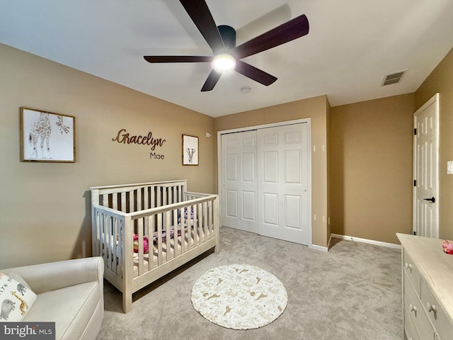 bedroom with a closet, light colored carpet, visible vents, a crib, and baseboards