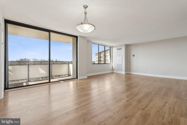 unfurnished room featuring a textured ceiling, a wall of windows, baseboards, and wood finished floors