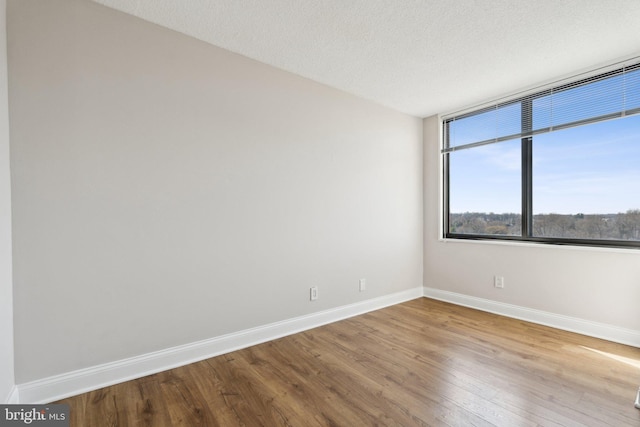 empty room with baseboards, a textured ceiling, and wood finished floors