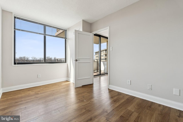 unfurnished room featuring a textured ceiling, baseboards, and wood finished floors