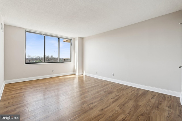 empty room with a textured ceiling, baseboards, and wood finished floors