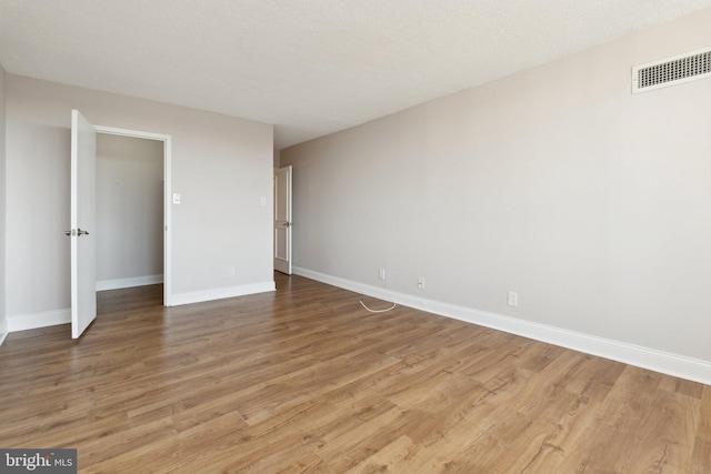 unfurnished room with light wood-style flooring, baseboards, visible vents, and a textured ceiling