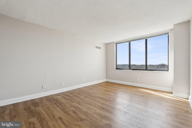 empty room with a textured ceiling, wood finished floors, visible vents, and baseboards