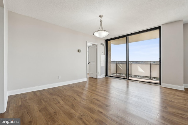 spare room featuring a wall of windows, baseboards, a textured ceiling, and wood finished floors