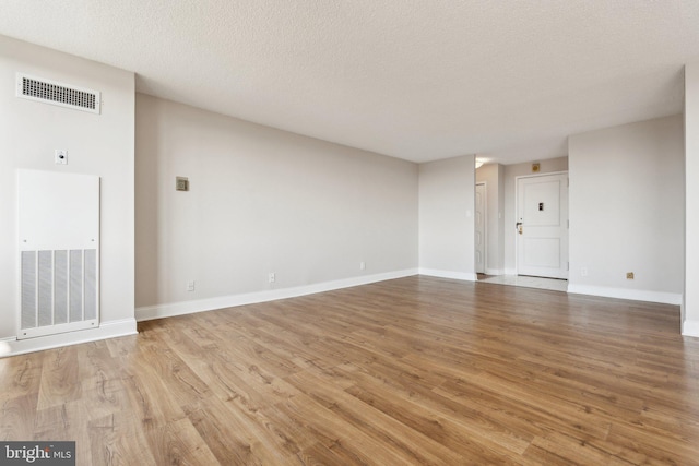 empty room featuring visible vents, baseboards, a textured ceiling, and light wood-style flooring