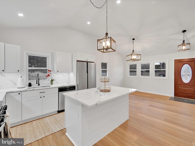 kitchen featuring stainless steel appliances, vaulted ceiling, a sink, light stone countertops, and light wood-type flooring