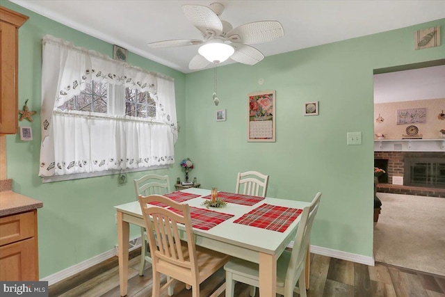 dining space with ceiling fan, a fireplace, baseboards, and wood finished floors