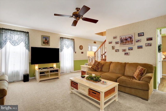 carpeted living area featuring stairs, ceiling fan, baseboards, and wallpapered walls