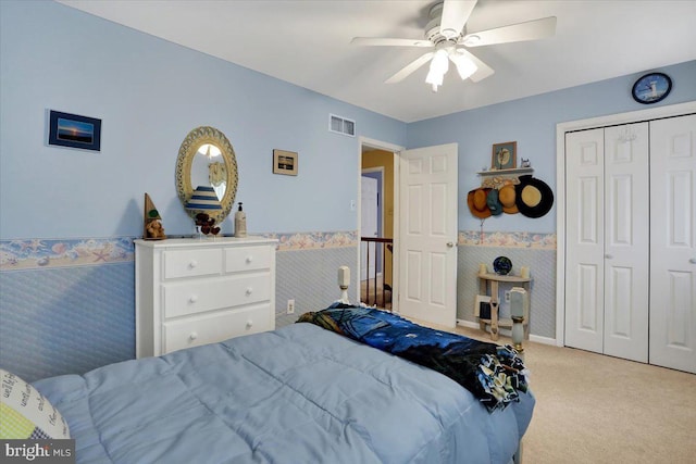 carpeted bedroom featuring wallpapered walls, visible vents, a ceiling fan, wainscoting, and a closet