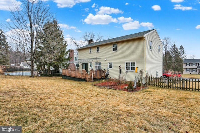 rear view of property featuring a chimney, a lawn, a deck, and fence