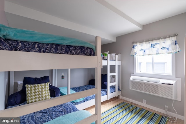 bedroom featuring a wall unit AC, wood finished floors, and baseboards