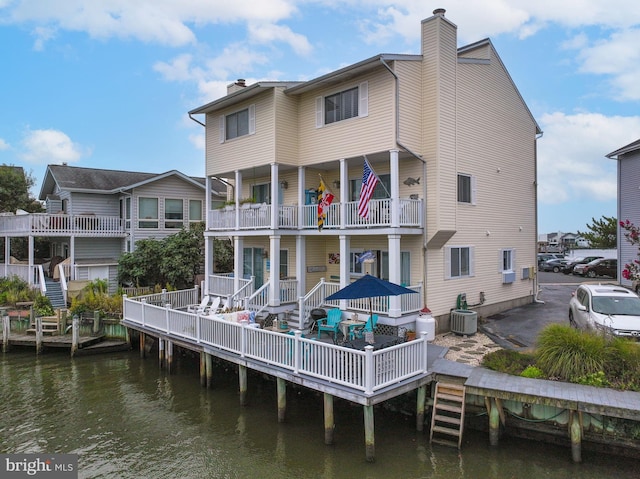 back of house with a balcony, a chimney, central AC unit, and a deck with water view