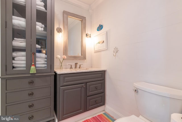 half bathroom with ornamental molding, vanity, and toilet