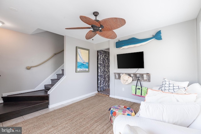 tiled living area featuring a ceiling fan, baseboards, and stairs