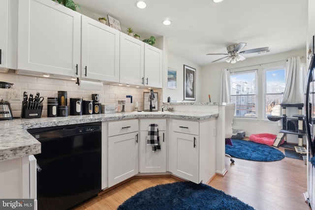 kitchen with a sink, white cabinetry, black dishwasher, light wood-type flooring, and tasteful backsplash