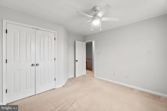 unfurnished bedroom with a closet, light carpet, ceiling fan, and baseboards