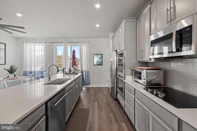 kitchen with appliances with stainless steel finishes, dark wood-type flooring, a sink, and gray cabinetry