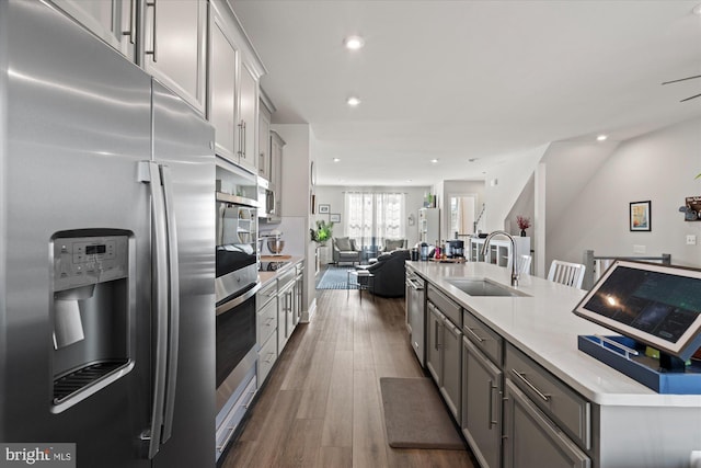 kitchen with a center island with sink, gray cabinetry, appliances with stainless steel finishes, open floor plan, and a sink