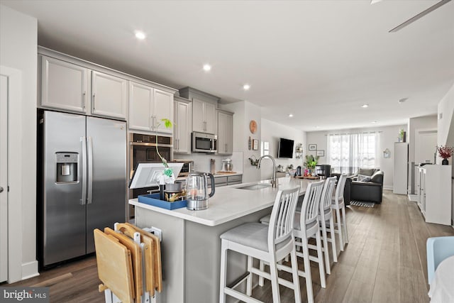 kitchen with gray cabinetry, a breakfast bar, a sink, open floor plan, and appliances with stainless steel finishes