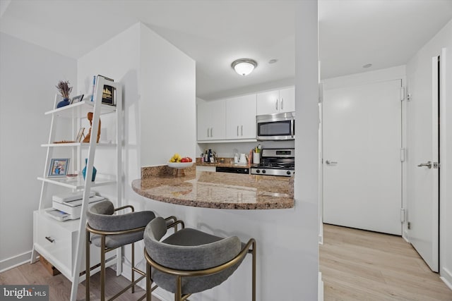 kitchen with stainless steel appliances, light wood-type flooring, white cabinets, and light stone countertops