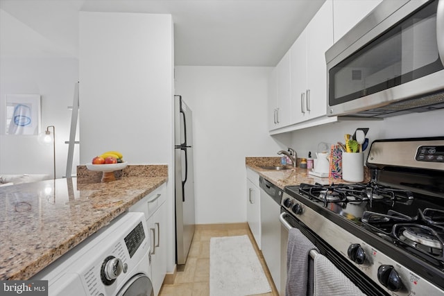 kitchen featuring white cabinets, appliances with stainless steel finishes, washer / clothes dryer, light stone countertops, and a sink