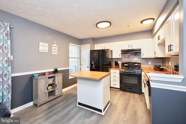 kitchen with under cabinet range hood, a sink, white cabinetry, light wood-type flooring, and black appliances