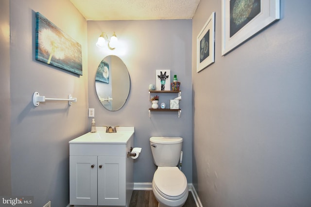 bathroom featuring toilet, vanity, a textured ceiling, wood finished floors, and baseboards