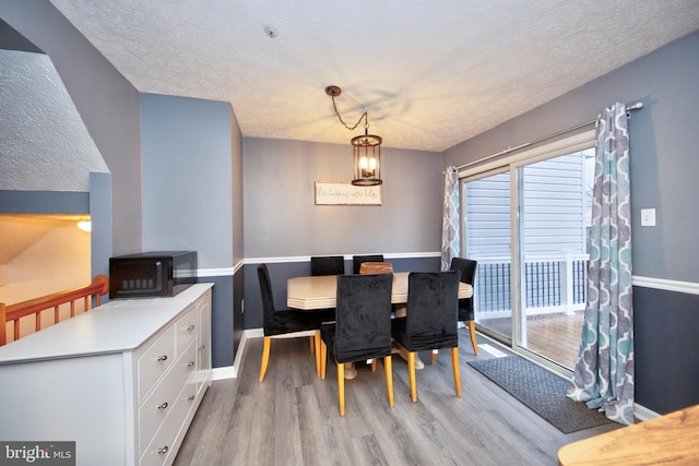 dining space with a textured ceiling, light wood-style flooring, and baseboards