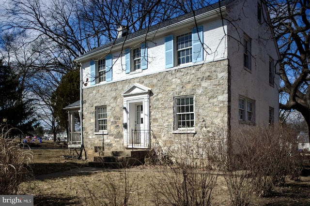 colonial home with stone siding and a chimney