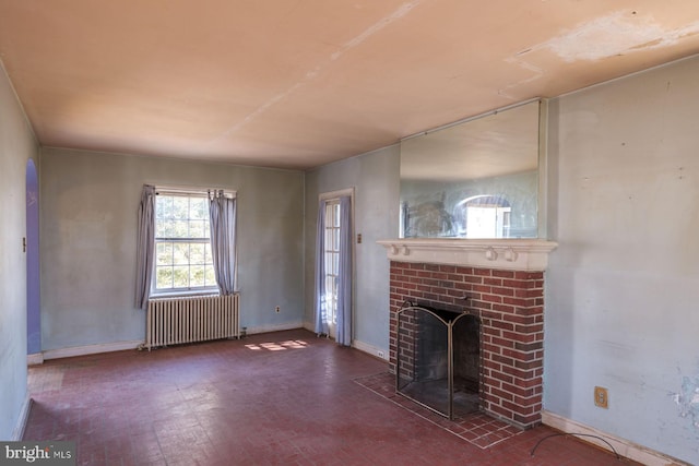 unfurnished living room featuring baseboards, brick floor, a brick fireplace, and radiator