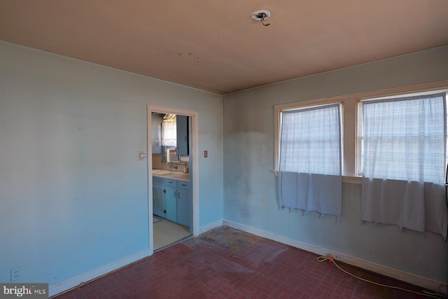 unfurnished room with a healthy amount of sunlight, brick floor, a sink, and baseboards