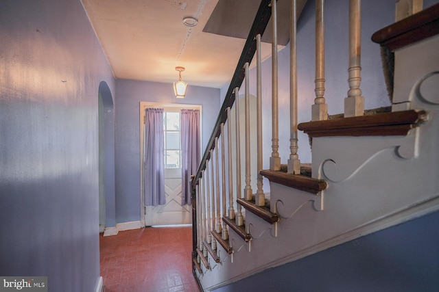 foyer entrance featuring brick floor, baseboards, stairs, and arched walkways