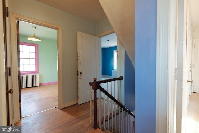 hallway featuring baseboards, wood finished floors, an upstairs landing, and radiator