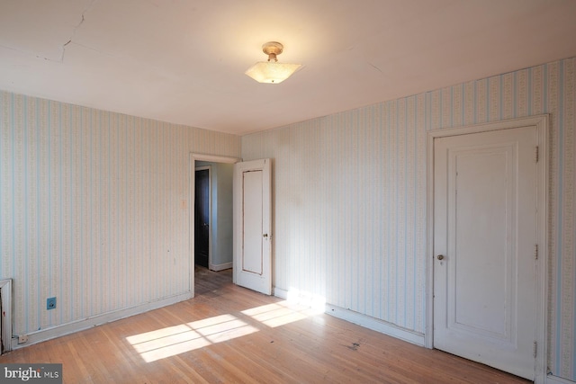 empty room with wood finished floors and wallpapered walls