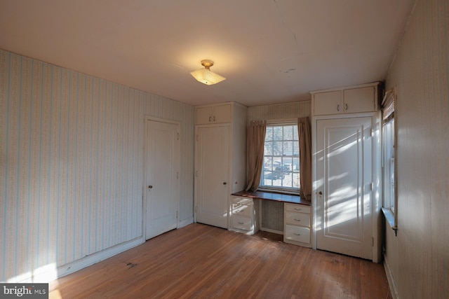 unfurnished bedroom with built in study area, light wood-style flooring, and wallpapered walls