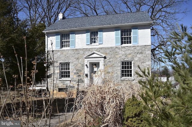 colonial home with stone siding, a chimney, and roof with shingles