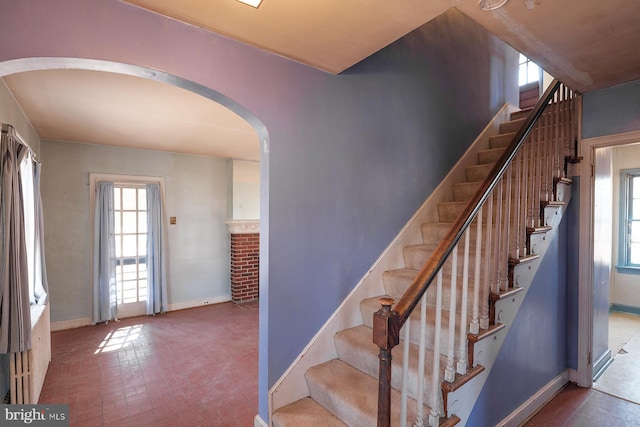 stairs with arched walkways, brick floor, and baseboards