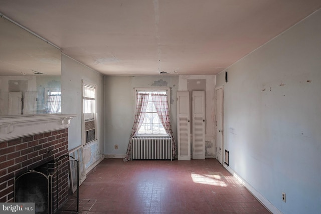 unfurnished living room featuring radiator heating unit, a brick fireplace, and baseboards