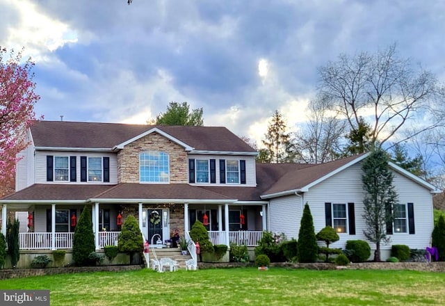 view of front of home featuring a front yard, stone siding, and covered porch